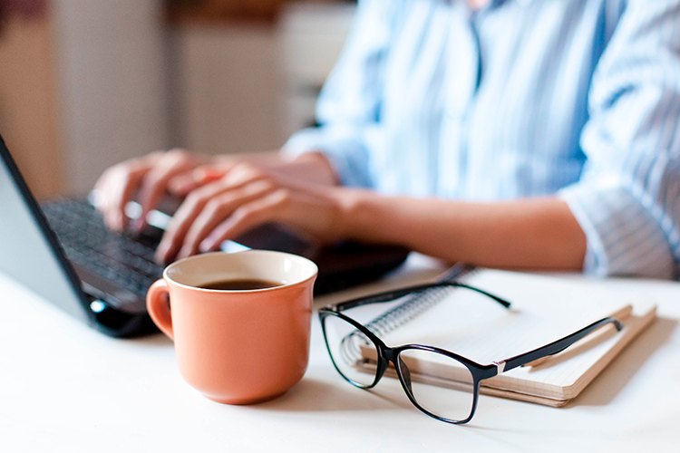 Pessoa ao computador com uma caneca de café e óculos, representando formas de otimizar o trabalho remoto